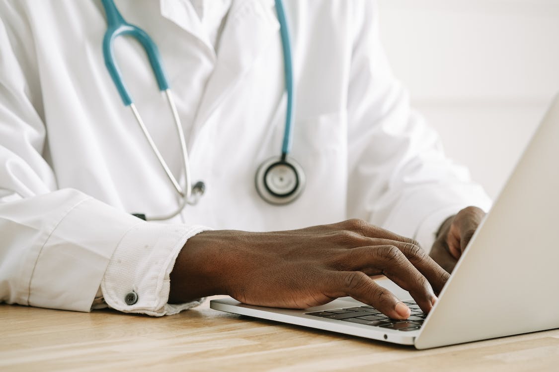 A doctor wearing a white coat and a stethoscope looking at a computer screen A doctor wearing a white coat and a stethoscope looking at a computer screen