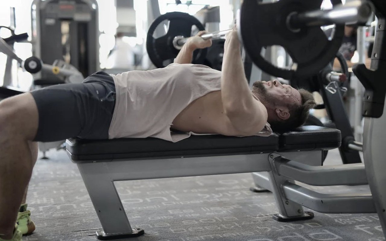 Strong sportsman working out on bench in modern gym